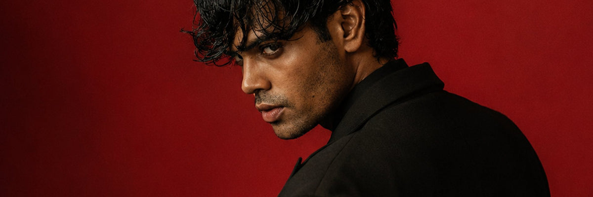 Man in a black jacket looking over his shoulder against a deep red backdrop